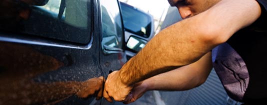 Homme en train d’entrer par effraction dans une voiture.