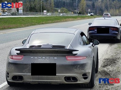 a black Porsche with a blue Audi parked on the side of the highway