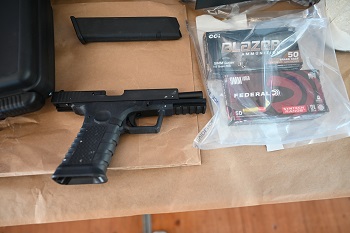 A black handgun, ammunition magazine and two boxes of ammunition in a clear bag laid out on a table.
