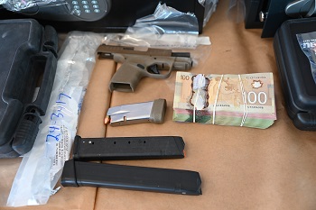 Three ammunition magazines, a brown handgun, and a wad of Canadian currency laid out on a table.