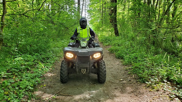 An officer is driving an ATV down a dirt path through a green space