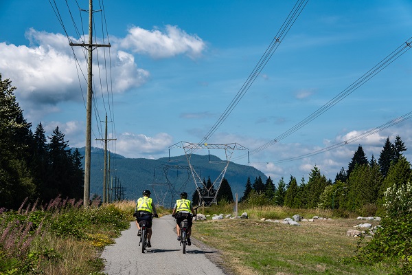 Two officers conduct bike patrols on a trail under power lines
