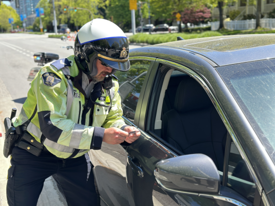 Un agent du Détachement de la GRC de Richmond portant un casque de moto vérifie le permis de conduire d’un conducteur à côté d’un véhicule