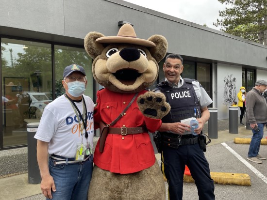 Un policier de la GRC de Richmond et un bénévole, accompagnés de l’Ours prudent, à l’extérieur du bureau de police communautaire