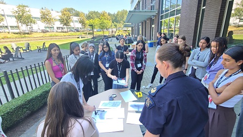 a group of female youth around a table, learning about the equipment used by RCMP Forensic Identification Services