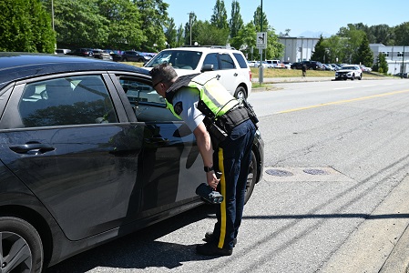 A police officer in uniform leans into the window of a pulled over car outside a school on a sunny day 