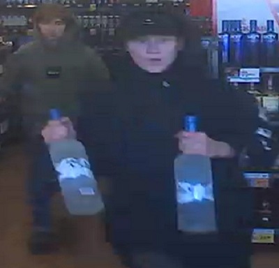 Male youth suspect wearing a black hoodie and a black ball cap carrying two large bottles of Grey Goose Vodka