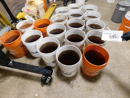 Three large orange plastic buckets and numerous large white plastic buckets, all willed with a brown liquid.