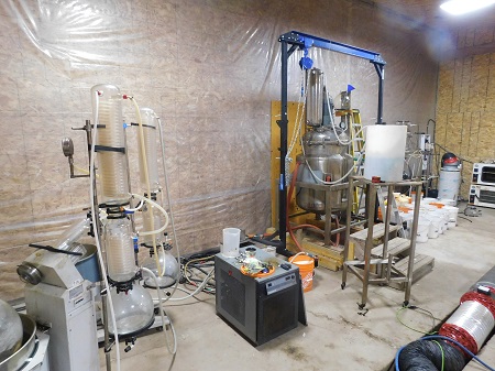 A large room with drug making materials, including giant glass beakers, and numerous large plastic buckets.