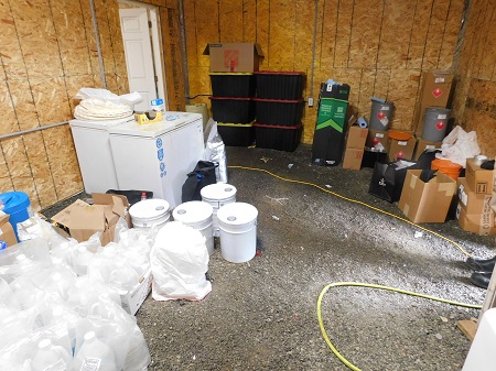 A storage room with two small deep freezers, different coloured large plastic buckets, storage totes and brown boxes.