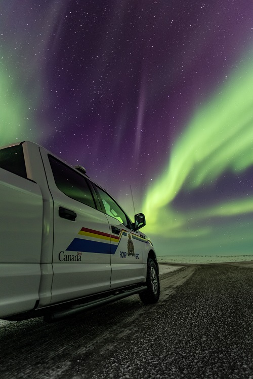 Camionnette de la GRC garée sur une route de gravier enneigée et aurores boréales en arrière-plan.