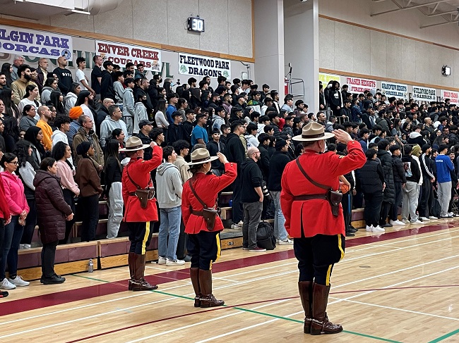 Photo de trois agents en tunique rouge saluant une grande foule dans les gradins.