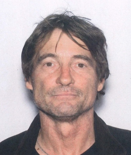 Caucasian man with short brown eyes, brown hair and a dark stubble beard, wearing a dark collared shirt.