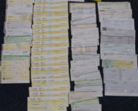 Numerous blurred fraudulent cheques displayed on the floor.