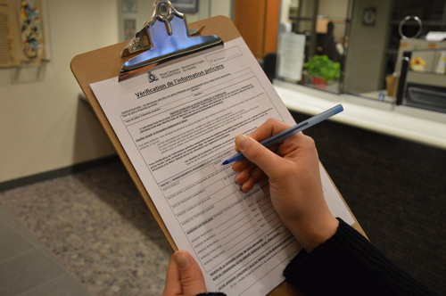 Image de la main droite d’une personne sur le point de remplir le formulaire Vérification de l’information policière sur une planchette à pinces.