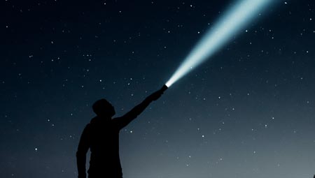 Silhouette d’une personne tenant une lampe de poche allumée dans la nuit.