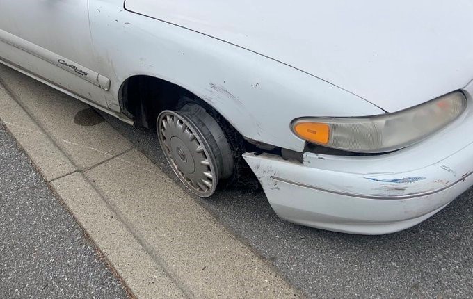 White car missing front passenger tire, metal rim exposed.