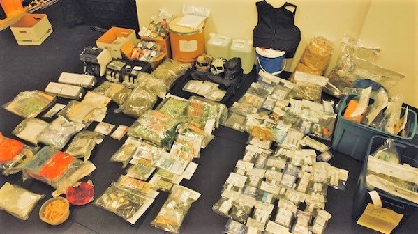 Packages of drugs and cash, money counters, body armour and skull-like face masks displayed across the floor