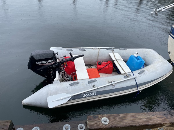 Grey ‘Grand’ inflatable with black Mercury outboard motor tied to the back of a sailboat