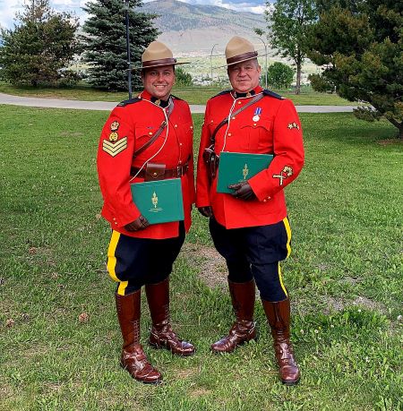 Two Mounties in red serge stand outside while holding their Queen’s Platinum Jubilee Awards.
