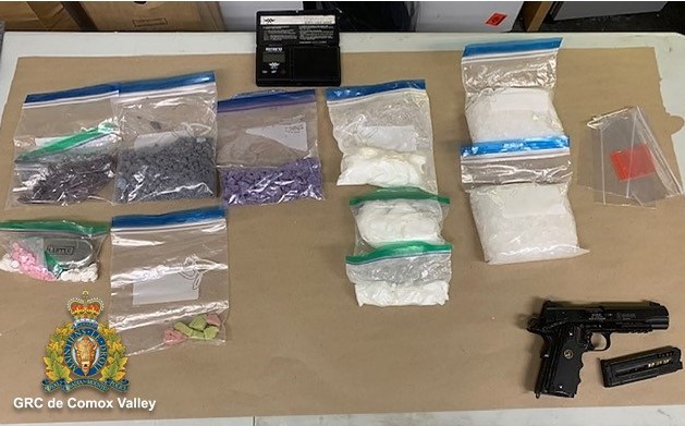 dix sacs à fermeture par pression et glissière disposés sur une table. Chaque sac contient des drogues illicites saisies par les enquêteurs. Il y a aussi une arme de poing noire et un chargeur à côté des sacs. 