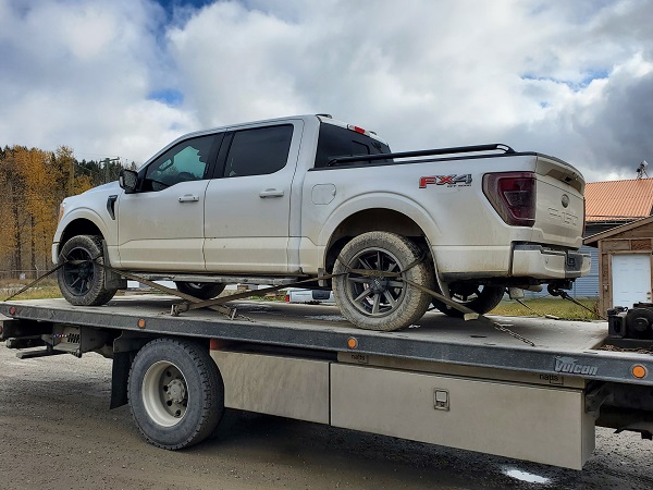 Image of a white Ford F150 pickup truck on the back of a flat deck tow truck.