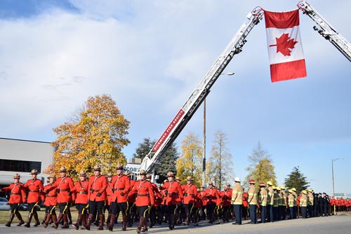 Des membres vêtus de la tunique rouge en train de marcher en dessus drapeaus du Canada