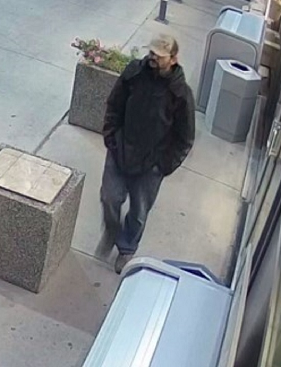 Suspect man with a dark coloured goatee wearing a black jacket, blue jeans and a brown and beige camouflage cap