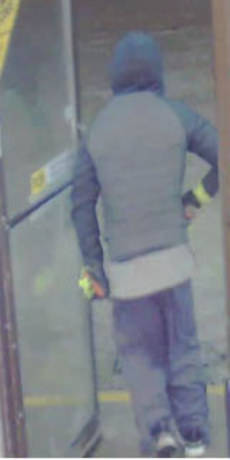 Suspect back: a man with a medium build walks out of a glass door, wearing a dark coat, pants, and gloves with fluorescent yellow on them.