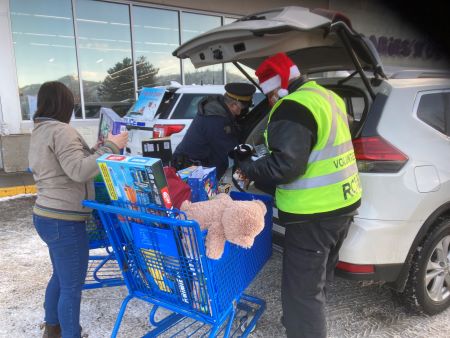 A woman offers a present to add to the shopping carts of gift donations being loaded into a van by a Kamloops police officer and a community policing volunteer. 