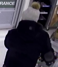 Photo du suspect captée de dos à l’aide d’une caméra de télévision en circuit fermé. Il porte un manteau à col haut et une tuque grise.