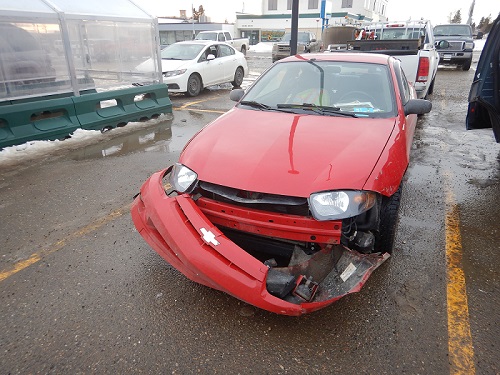 Voiture Chevrolet Cavalier rouge garée dans un stationnement et dont le pare-chocs est arraché.