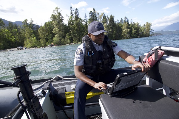 Cst Berthier Kyobela works on a laptop while seated in the BC RCMP Zodiac boat on Harrison Lake at Limbert Rocks Campsite. 