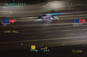 Aerial view from helicopter showing police vehicle behind black car on highway shoulder