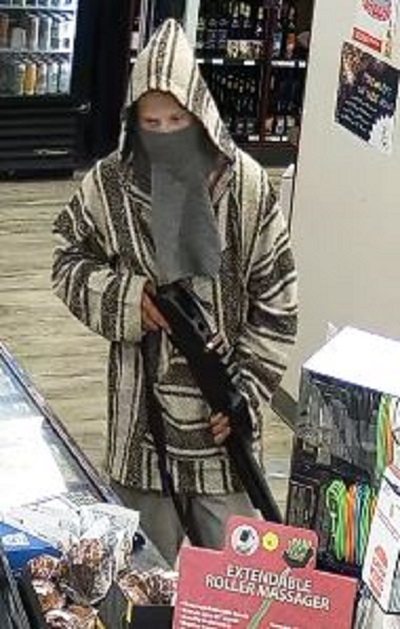 Male robbery suspect wearing a brown and beige vertical striped Mexican style poncho with a grey balaclava, holding a black shotgun with a single red shell in the top of the gun