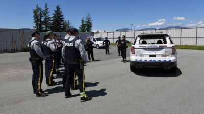 Groupe de policiers qui se tiennent près d’un véhicule de police et qui écoutent un instructeur donnant des instructions de formation.