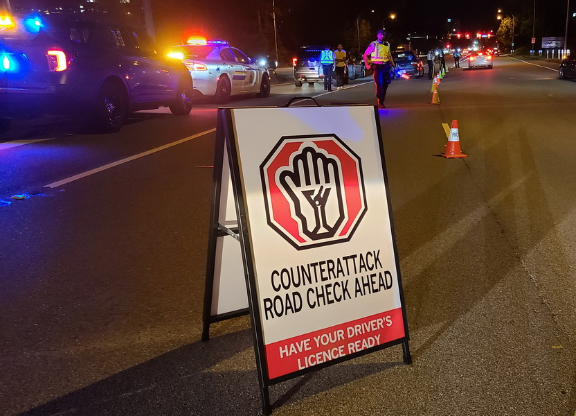 photo : panneau « Counter-Attack Road Check » sur la route, voitures de police aux gyrophares activés et cônes de signalisation en arrière-plan