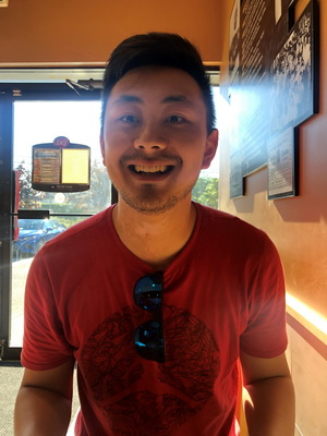 Photo of Ryan Liu with red t-shirt in an orange room with light shining through glass window