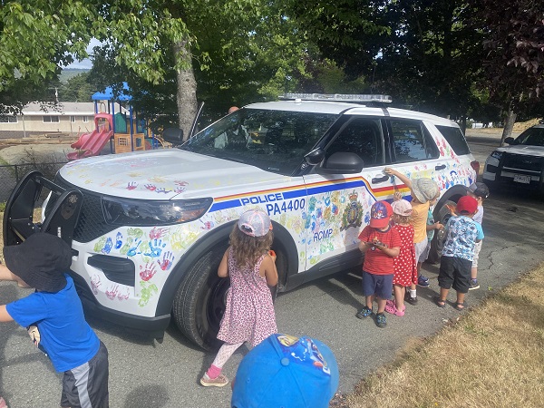 Several children paint an RCMP police car with hand prints