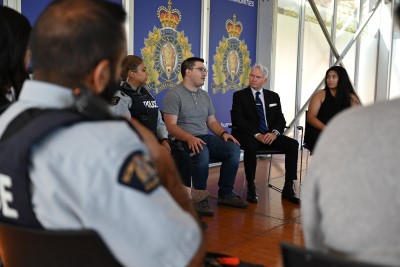An image showing the back of a police officer and several people in plainclothes sitting in chairs in a circle in a building with RCMP logos