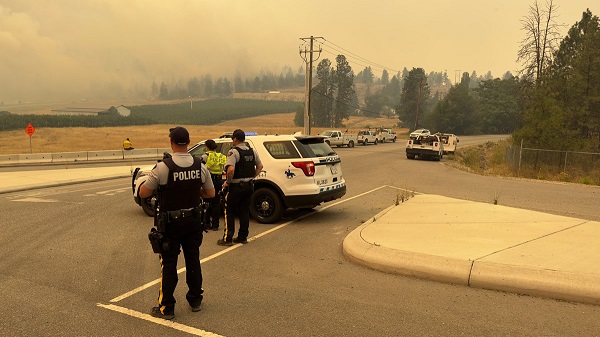 À un point de contrôle, des agents regardent un nuage de fumée provenant d’un incendie de forêt situé tout près