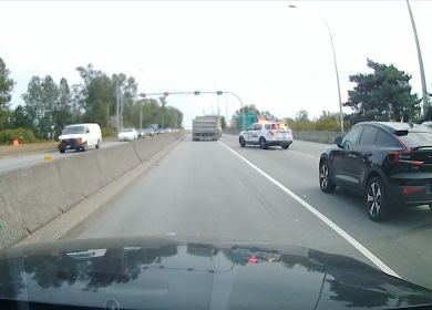 Vue arrière du camion à benne franchissant la ligne continue de gauche à droite; un véhicule de police identifié est derrière le camion et l’arrête