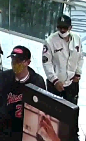 1)&#9;Deux hommes se promènent dans un centre commercial. L’un d’entre eux porte une casquette de baseball foncée des Dodgers de Los Angeles, un masque médical blanc, un blouson aviateur blanc arborant l’écusson des Bulls de Chicago ainsi qu’un pantalon noir. L’autre homme porte une casquette de baseball foncée arborant un logo rouge, une veste grise ainsi qu’une chemise foncée portant l’inscription « Chicago » et le numéro 23 à l’avant.