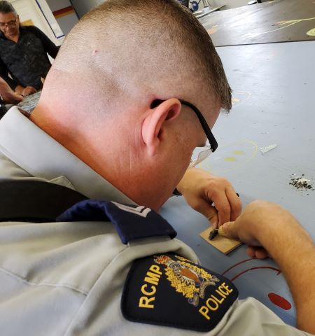 Taille de silex : Plan par-dessus l’épaule d’un policier en uniforme qui taille un morceau d’obsidienne. 