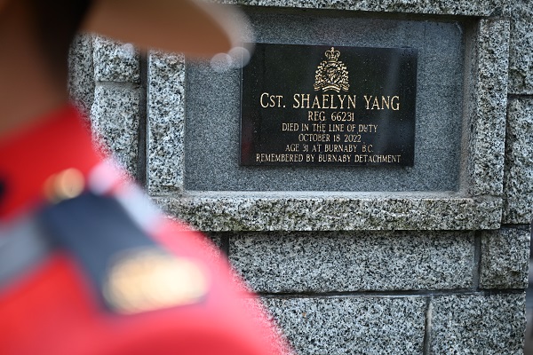 Le nom de la gendarme Shaelyn Yang sur une plaque noire sur un cairn en pierres à côté d’un agent de la GRC portant la tunique rouge