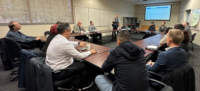 Male RCMP officers speaking to a group of stakeholder who are sitting around a boardroom table.