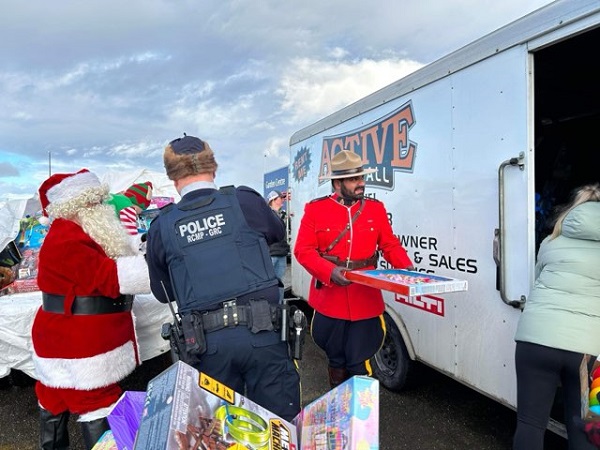 A police officer in red serge, a police officer in uniform, Santa Clause and a helper unloading donated items