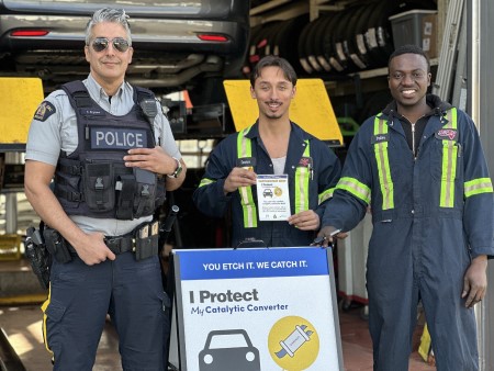 Photo of RCMP officer and mechanics standing in front of auto shop