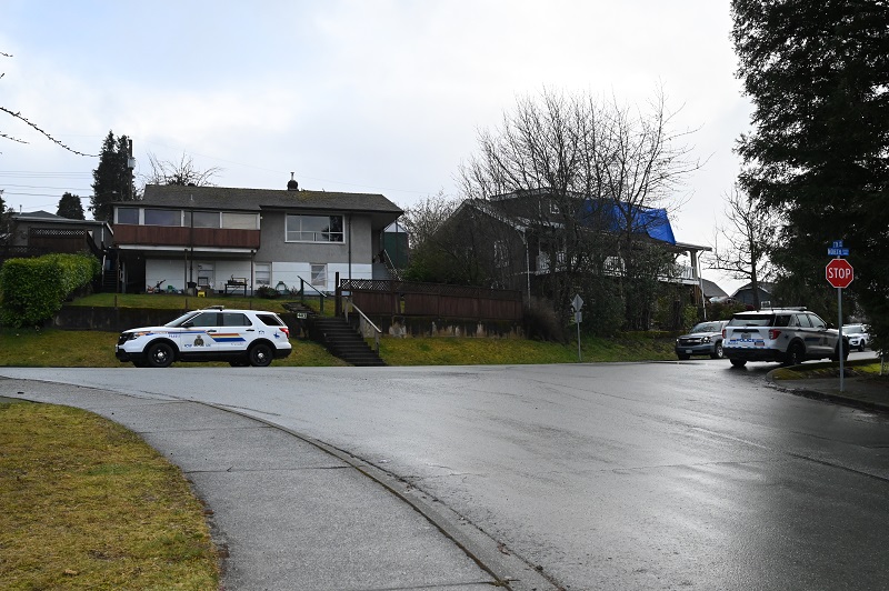 Police vehicles parked at an intersection,on a hill, in front of a house.